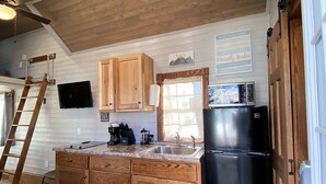 Una cocina con armarios de madera, un refrigerador negro y una ventana con cortinas.