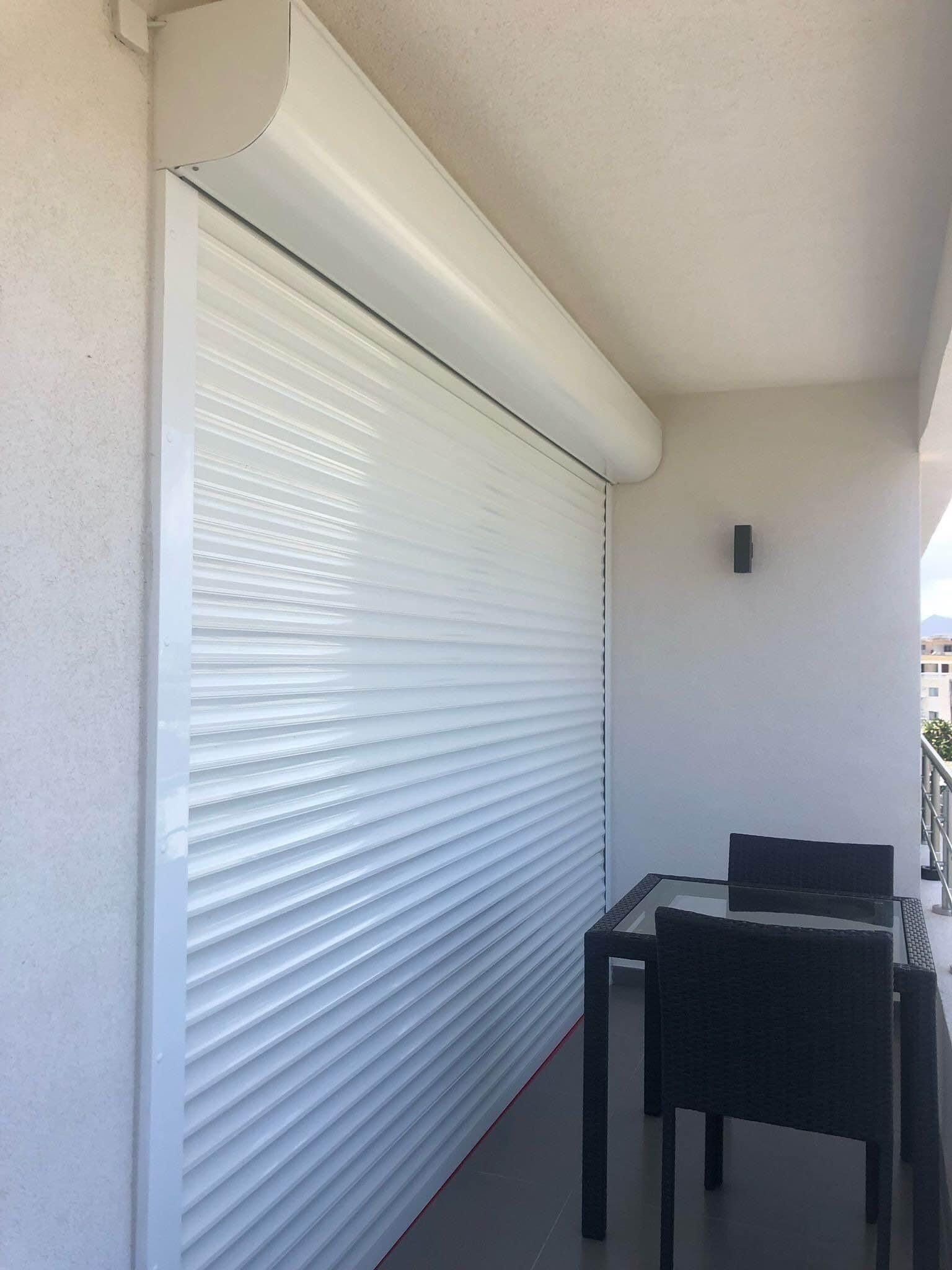 Uma varanda com toldo branco retrátil, uma mesa pequena e uma cadeira.