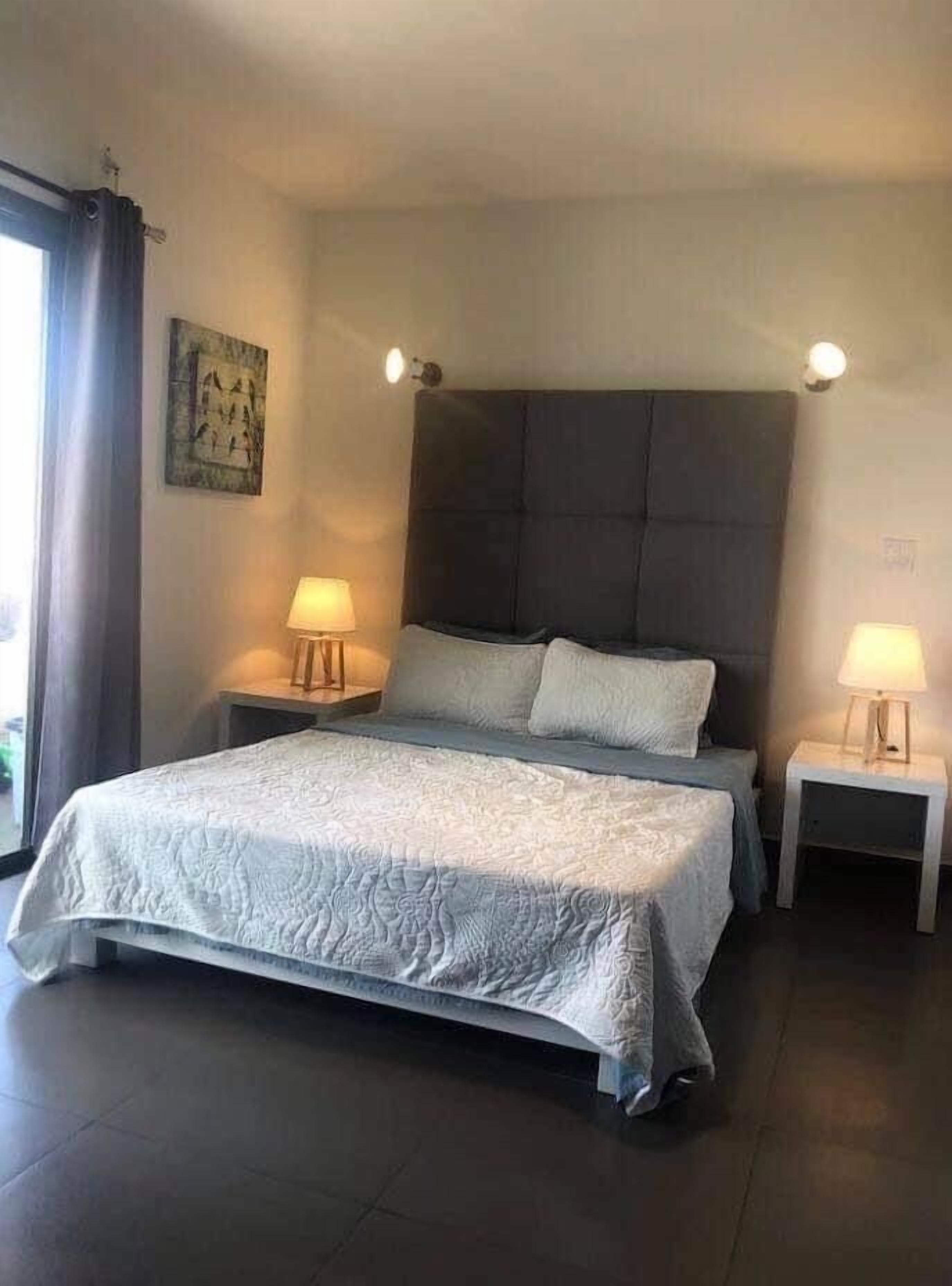 A bedroom with a large bed, two bedside tables with lamps, a headboard, and a painting on the wall.