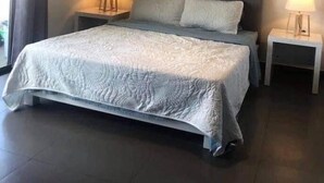 Un dormitori amb un llit gran, dues taules de nit amb làmpades, un capçal de llit i un quadre a la paret.