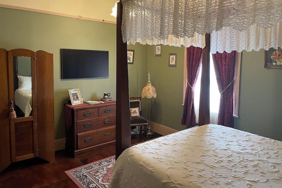 Une chambre à coucher avec un lit à baldaquin, une commode, un miroir et un téléviseur fixé au mur.