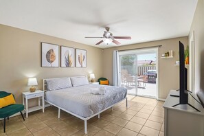 A bedroom with a bed, a ceiling fan, a TV, a desk, and a sliding glass door leading to an outdoor area.