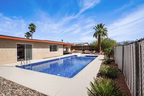 A swimming pool with a wooden deck, a fenced area, and a building with a red roof.