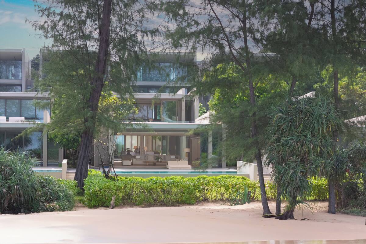 A modern beachfront property with a pool, outdoor seating, and lush greenery.