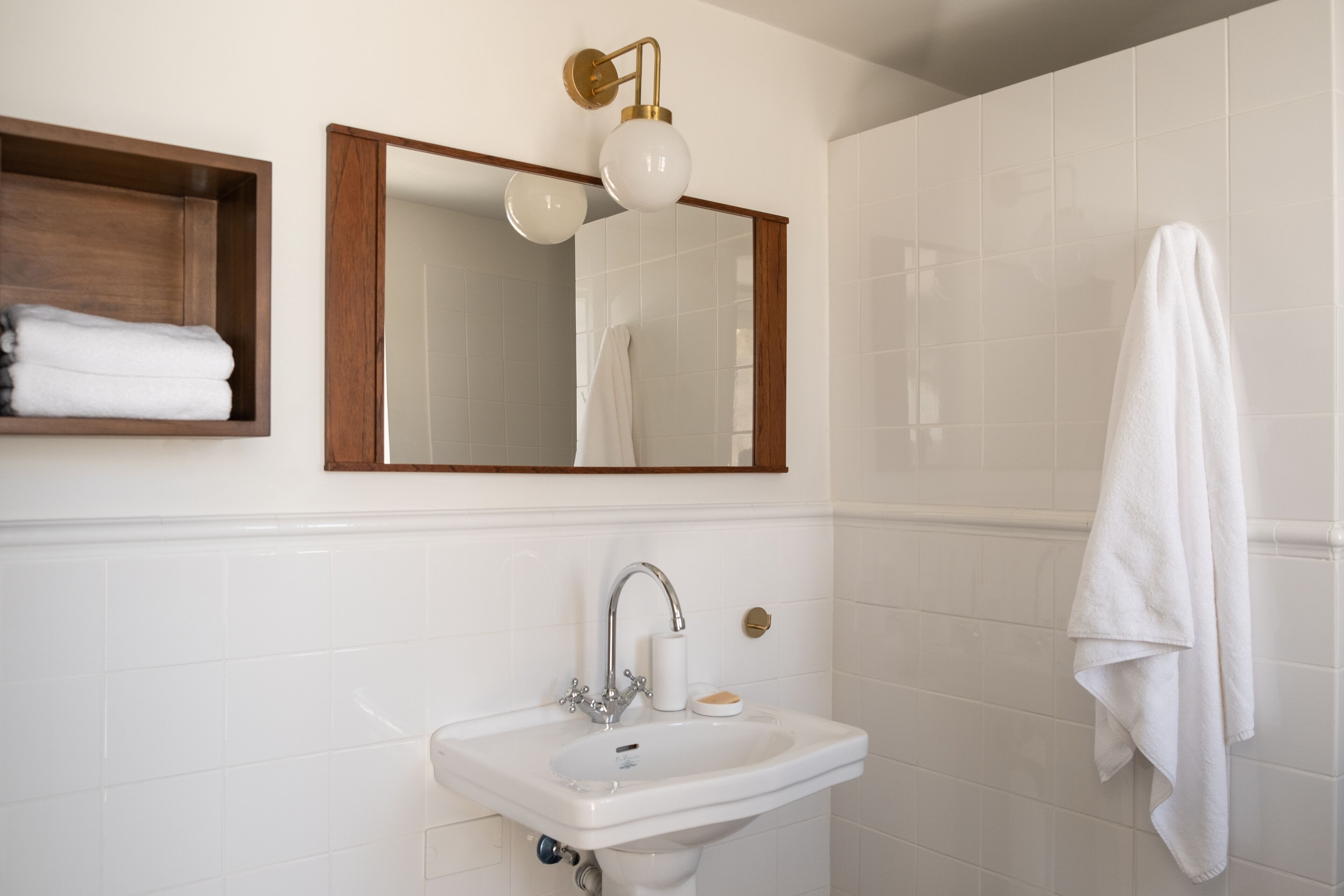 A bathroom with a white sink, a mirror, and a towel hanging on the wall.