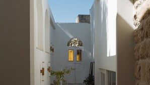 A narrow, white-walled corridor with a stone wall on one side and a door at the end. - KHAN EIN KAREM BOUTIQUE HOTEL (Jerusalem)