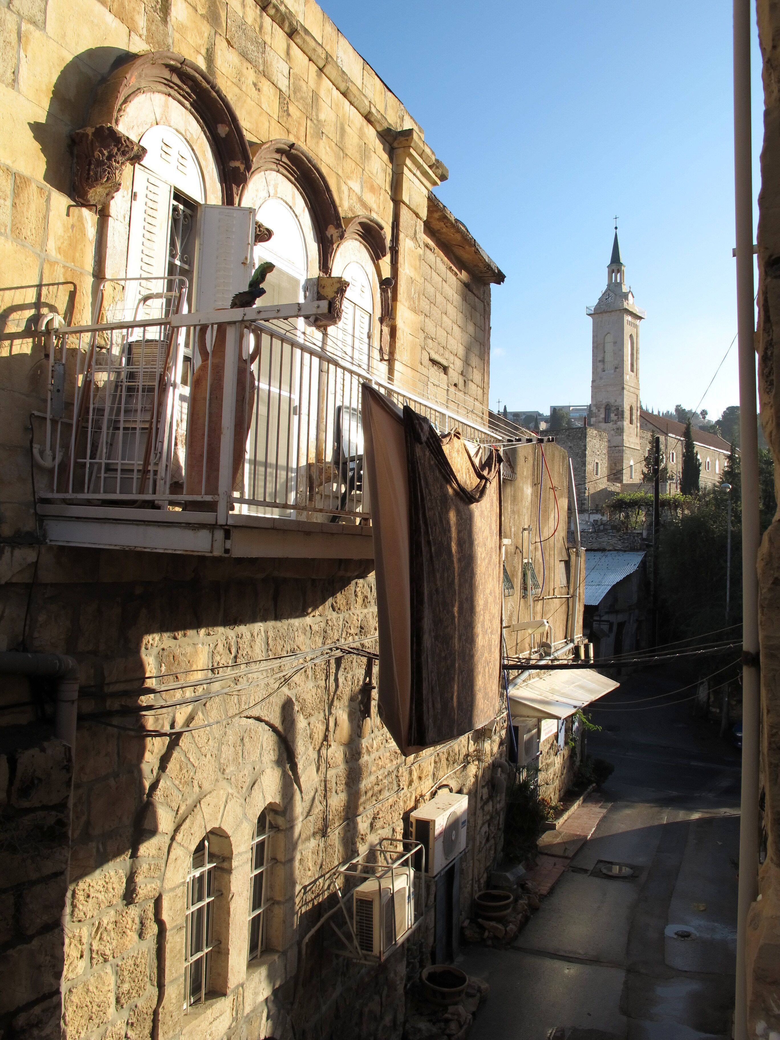 A historic building with a balcony, stone walls, and a clock tower in the background.