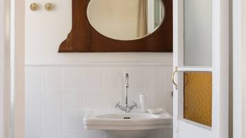 A bathroom with a pedestal sink, a wooden stool, a mirror with a gold frame, and a white door with a frosted glass panel.