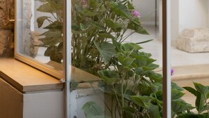 A modern interior with a stone wall, a glass window, and a view of a staircase and a room with a table and chairs. - KHAN EIN KAREM BOUTIQUE HOTEL (Jerusalem)