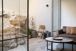 Een moderne woonkamer met een glazen scheidingswand, een stenen muur, een houten stoel, een bank en een bijzettafeltje.