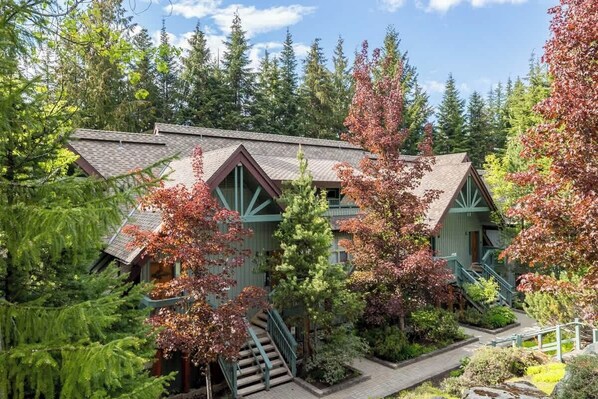 A lodge with a steeply pitched roof, a staircase leading to the entrance, and surrounded by dense forest.