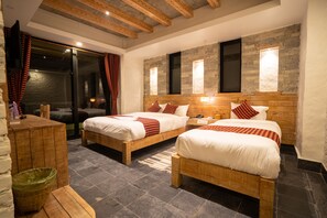 Habitació d'hotel amb dos llits de fusta, una paret de pedra i una porta de vidre que dona a un balcó.