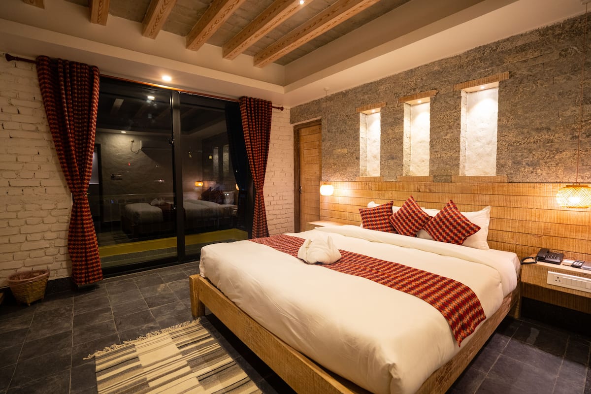 A modern hotel room with a large bed, a wooden headboard, and a stone accent wall.
