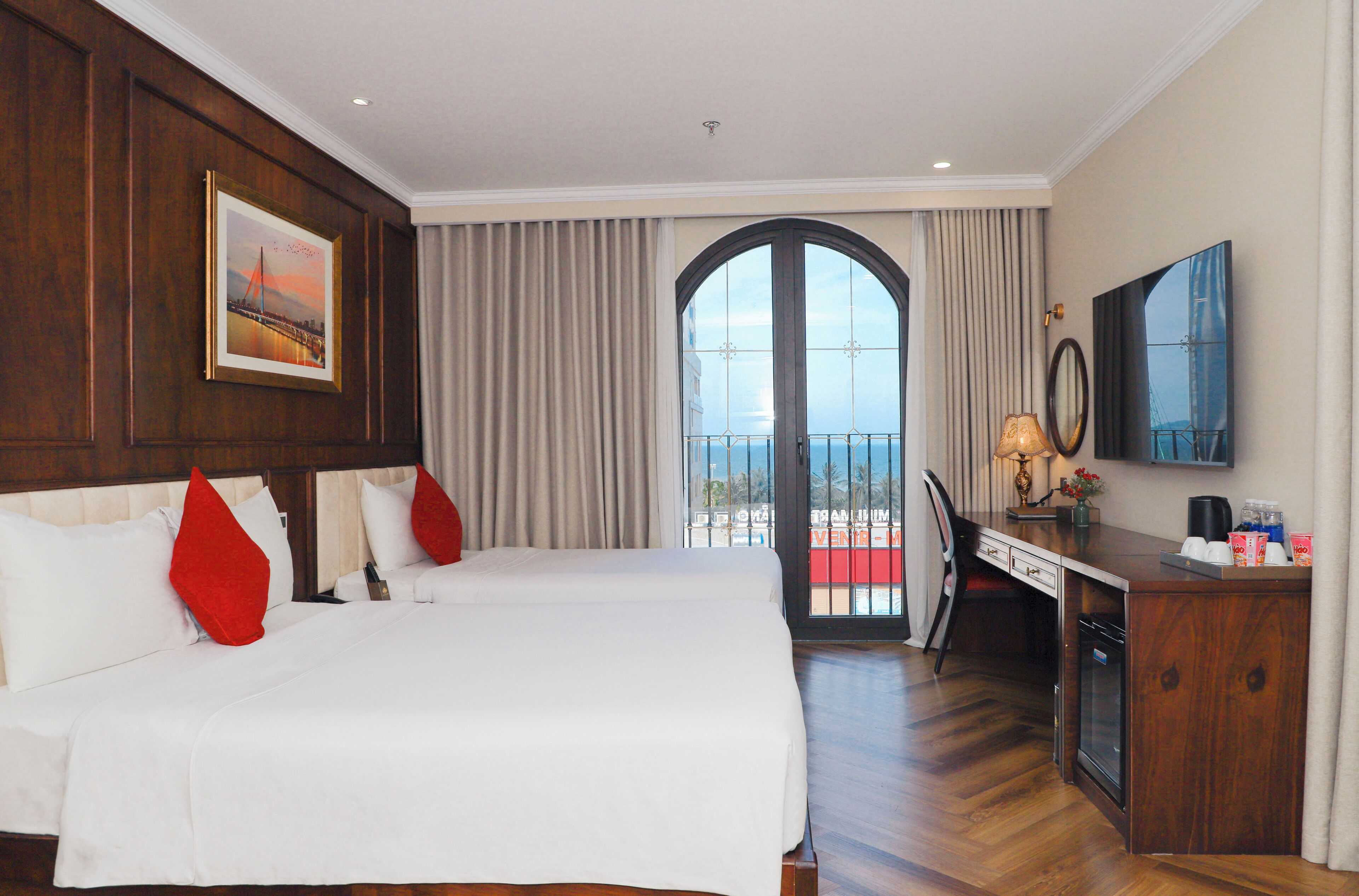 Habitación de hotel con dos camas, un escritorio con silla, televisor y balcón con vistas.