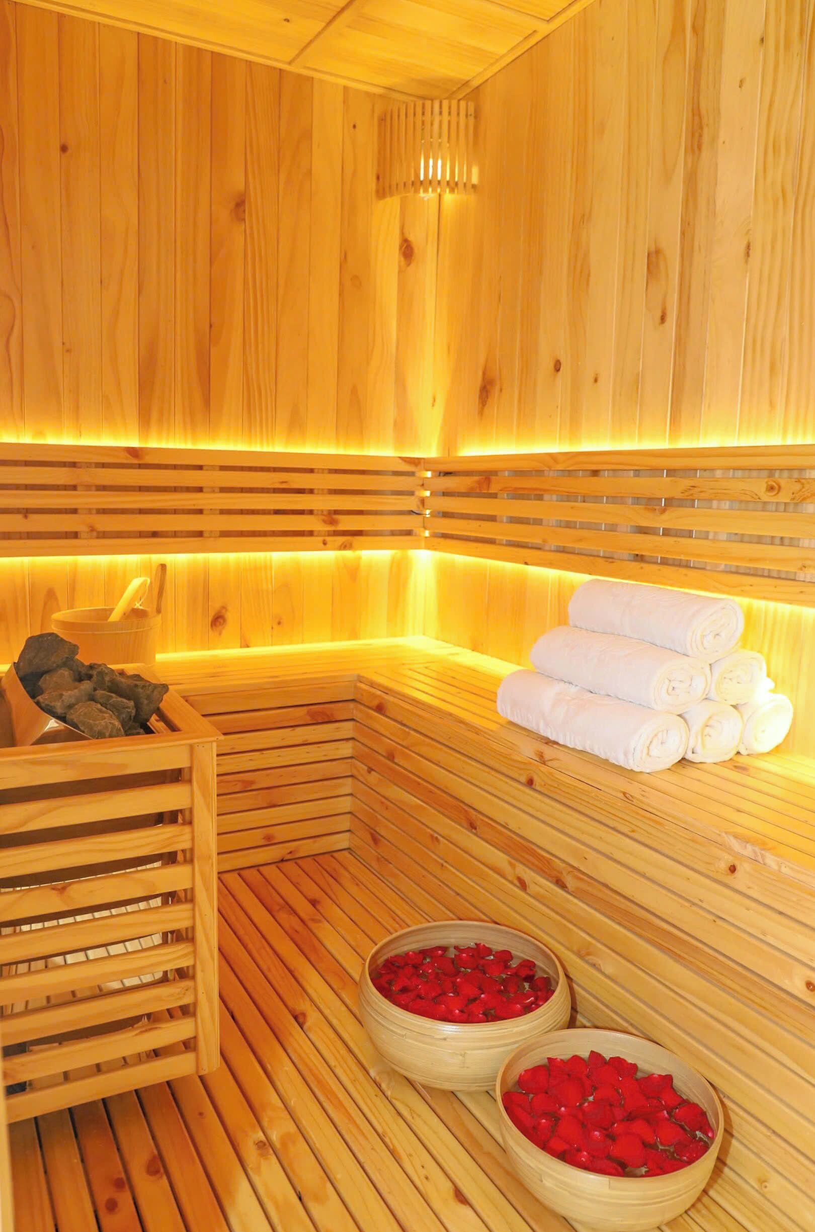 Una sauna de madera con bancos, un banco de madera con toallas y dos cuencos con flores rojas.