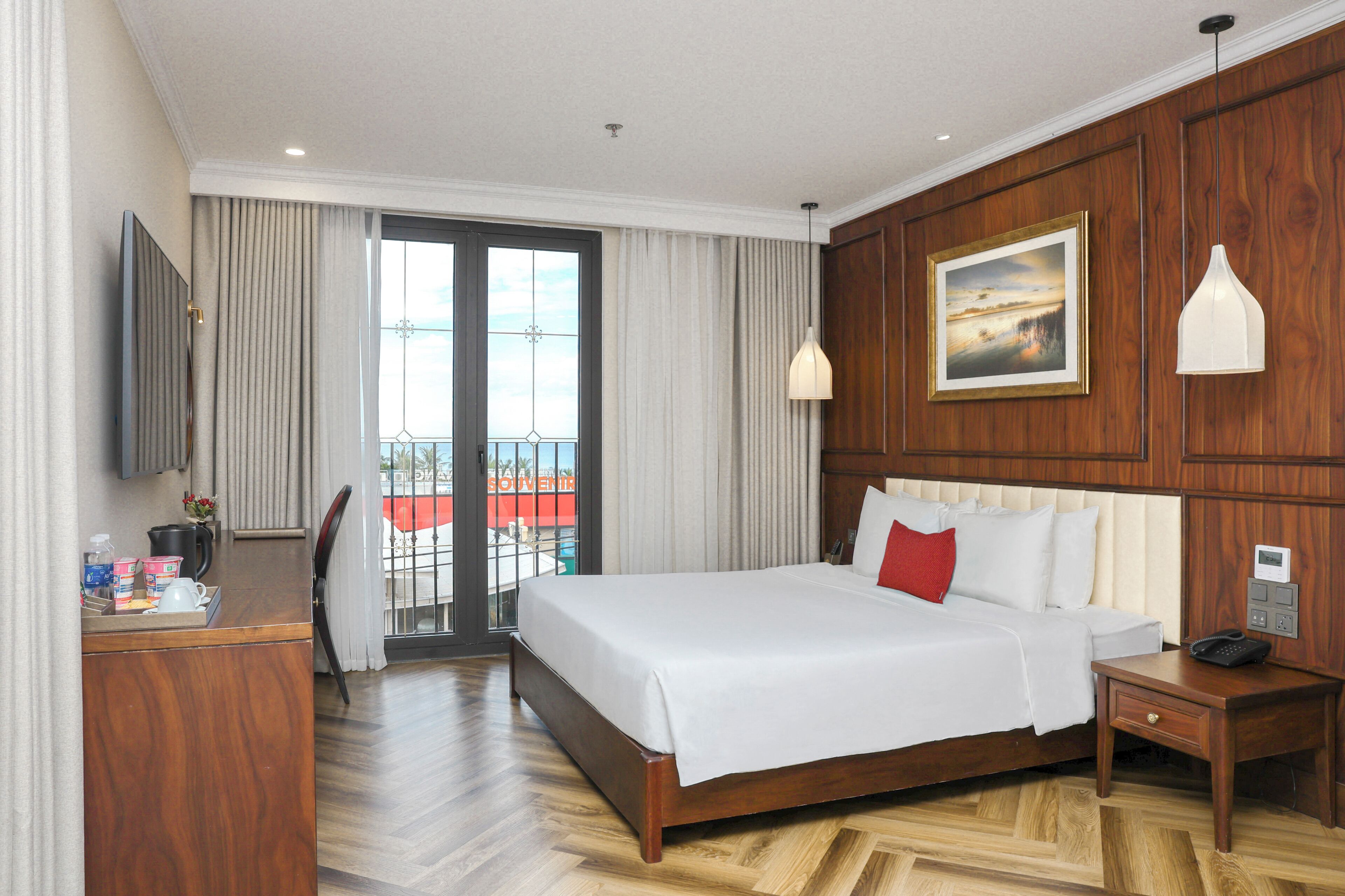 A hotel room with a large bed, wooden paneling, a TV, a desk with toiletries, and a balcony with a view.