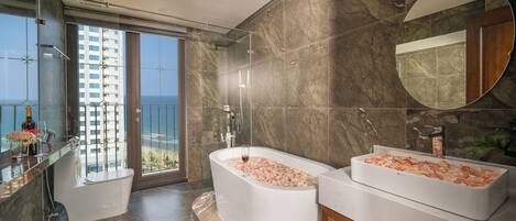 Un bagno moderno con una vasca da bagno grande piena di petali di rosa, un’area doccia separata e un vanità con uno specchio ampio.