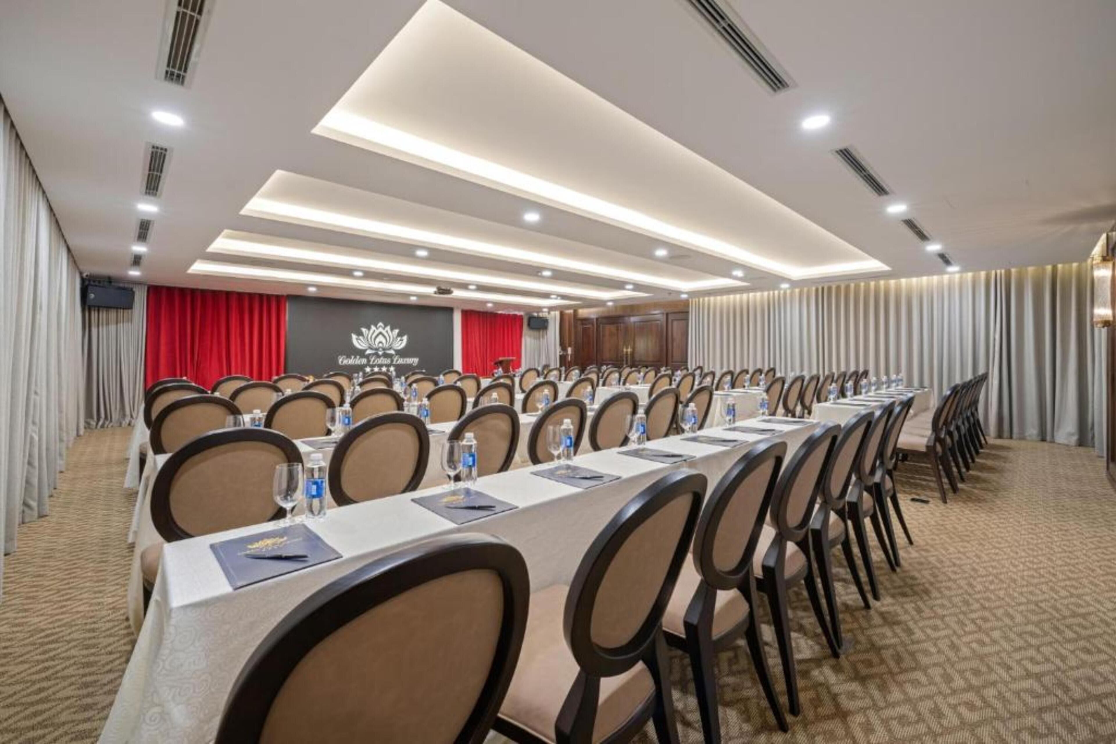 A conference room with long tables, chairs, and a stage with curtains.