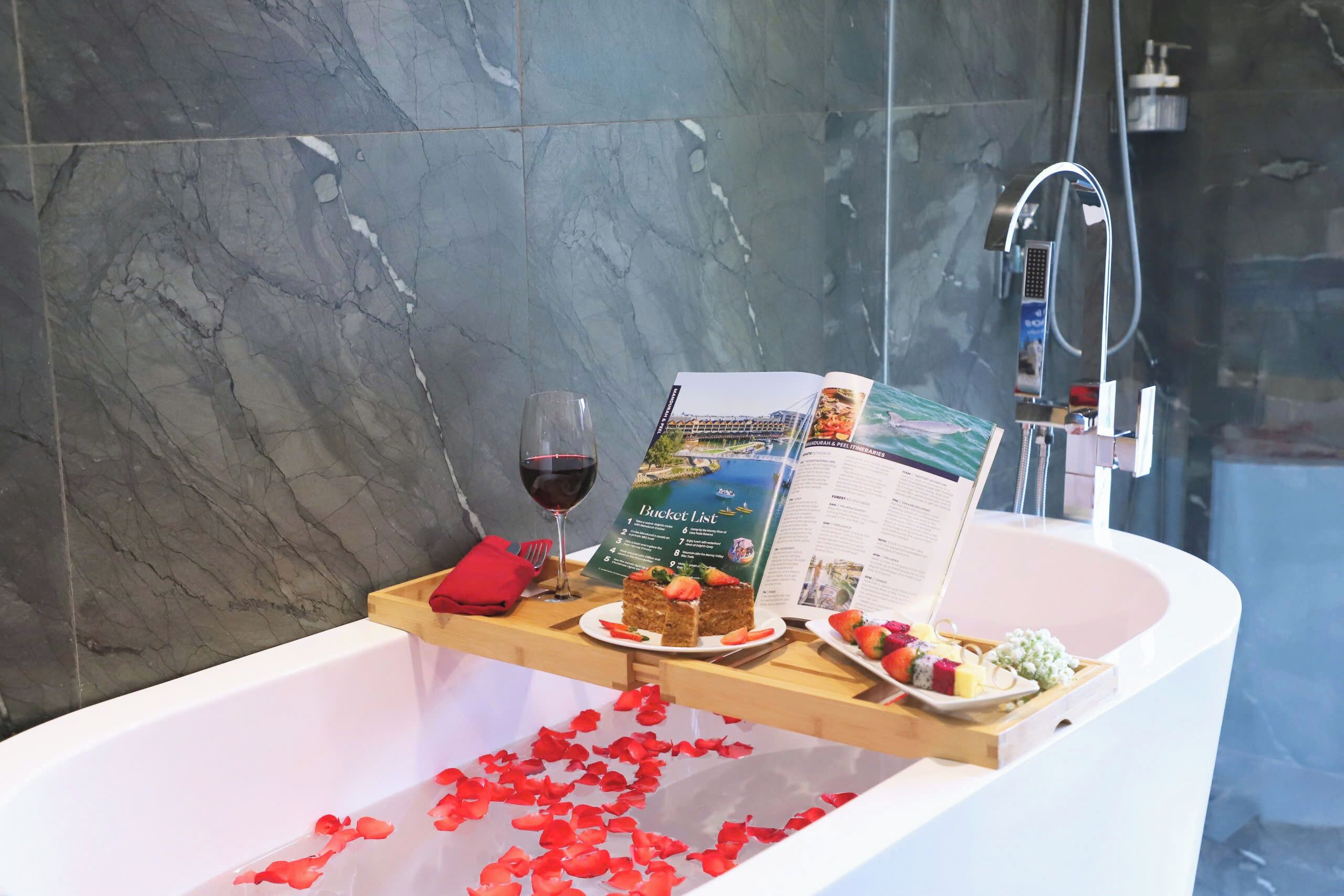 Una bañera con pétalos de rosa, una copa de vino tinto y un cartel con deseos por cumplir.