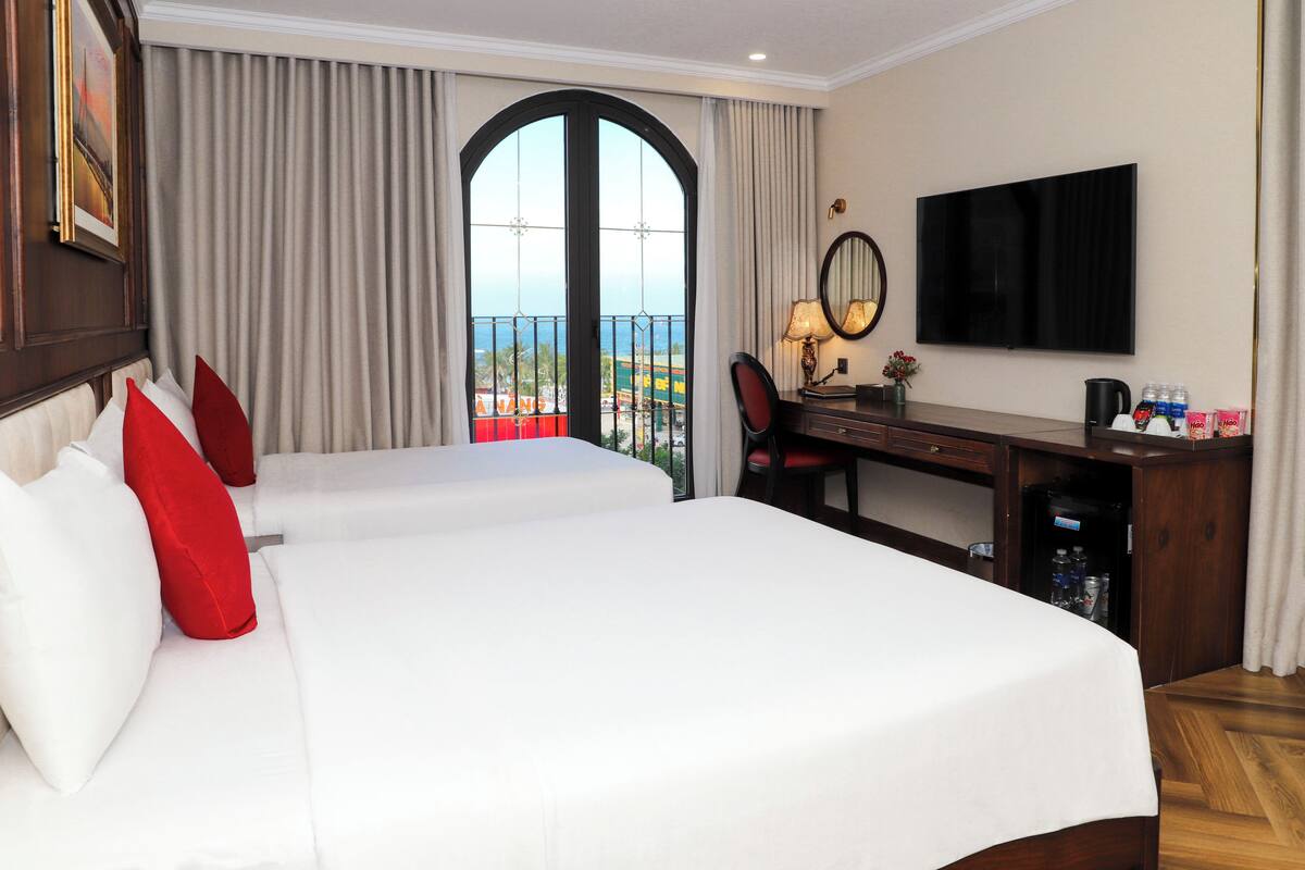A hotel room with a large bed, a desk with a chair, a television, and a view of the ocean.