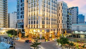 A multi-story hotel with a modern design, featuring a prominent corner entrance and a well-lit facade. - Golden Lotus Luxury Hotel Da Nang (Da Nang)