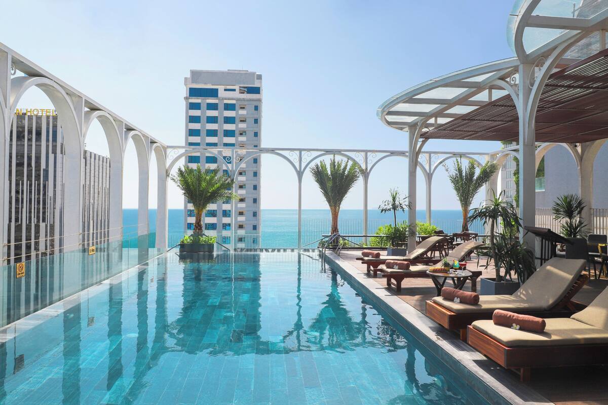A pool area with lounge chairs and a view of the ocean.