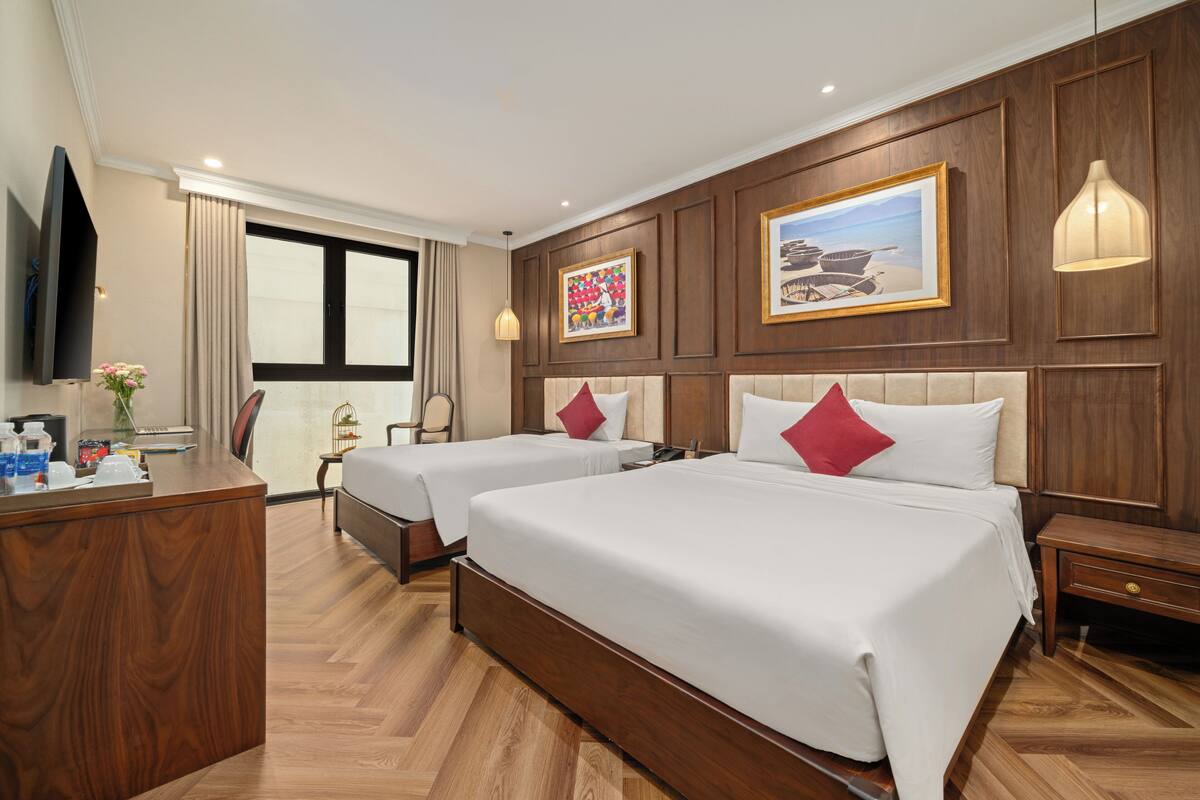 A hotel room with two beds, a desk, a TV, and a window with curtains.