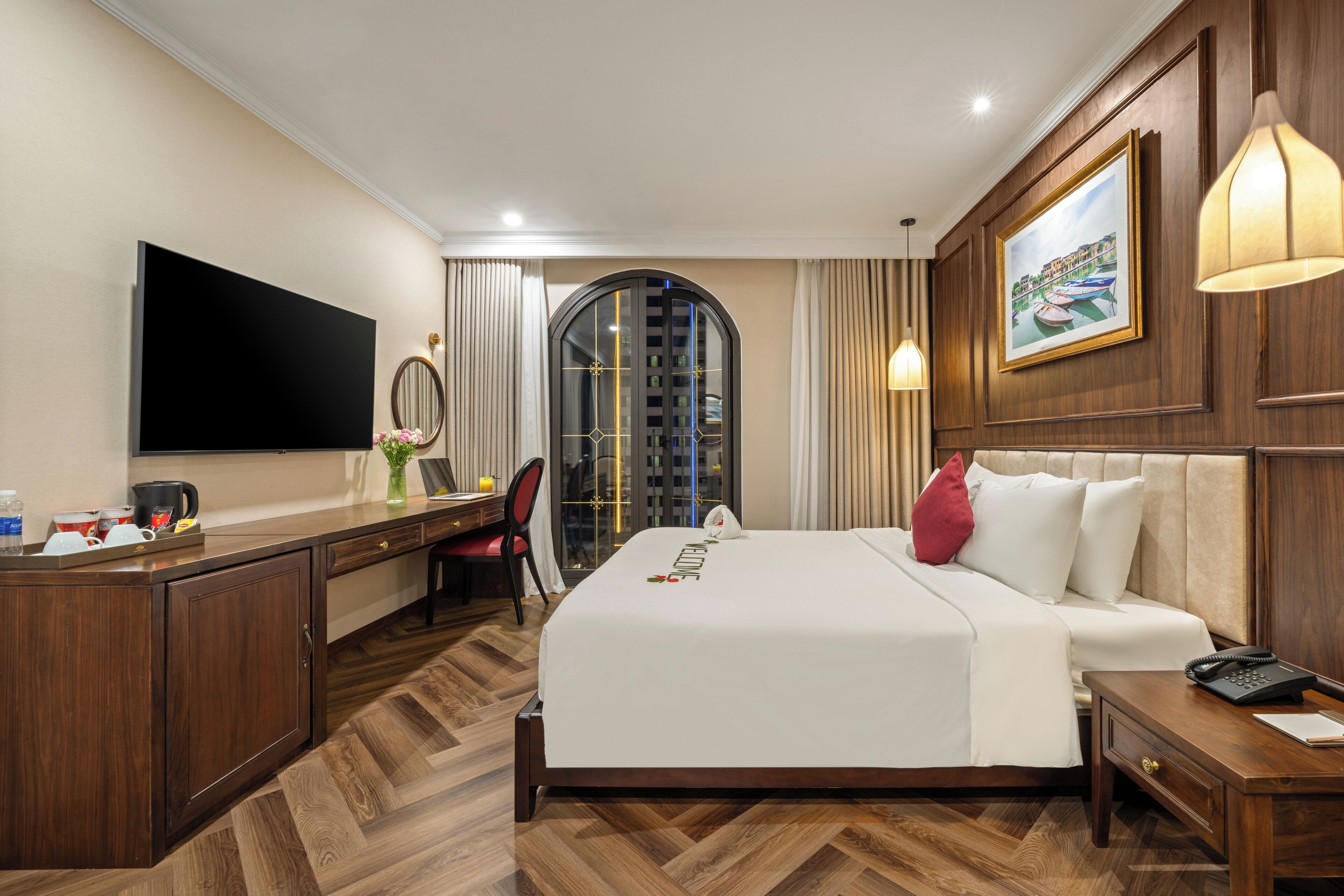 Hotelkamer met groot bed, bureau met stoel, flatscreen televisie, schilderij aan de muur en uitzicht door het raam.