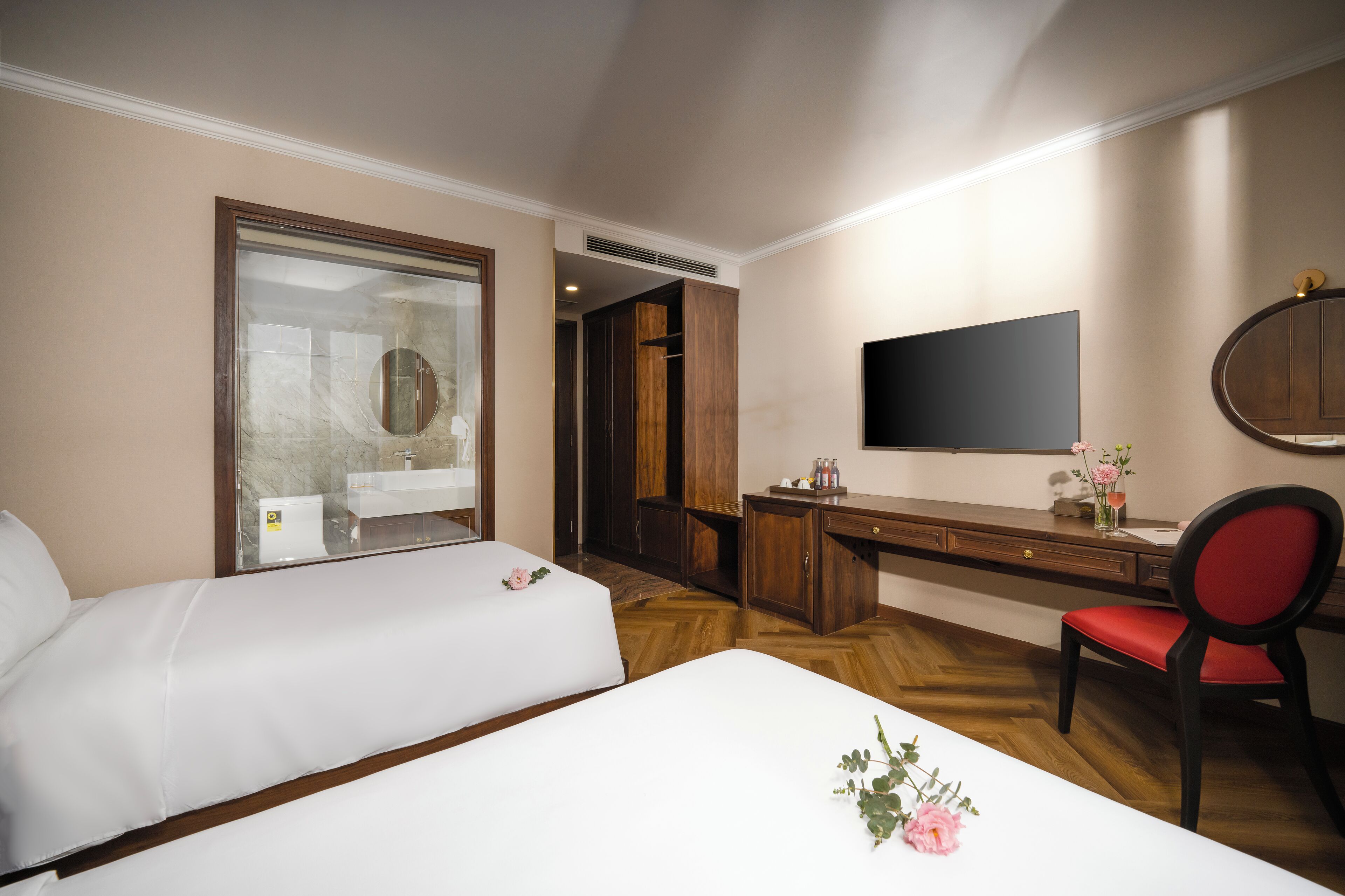 A hotel room with two beds, a desk, a chair, a TV, and a wardrobe.