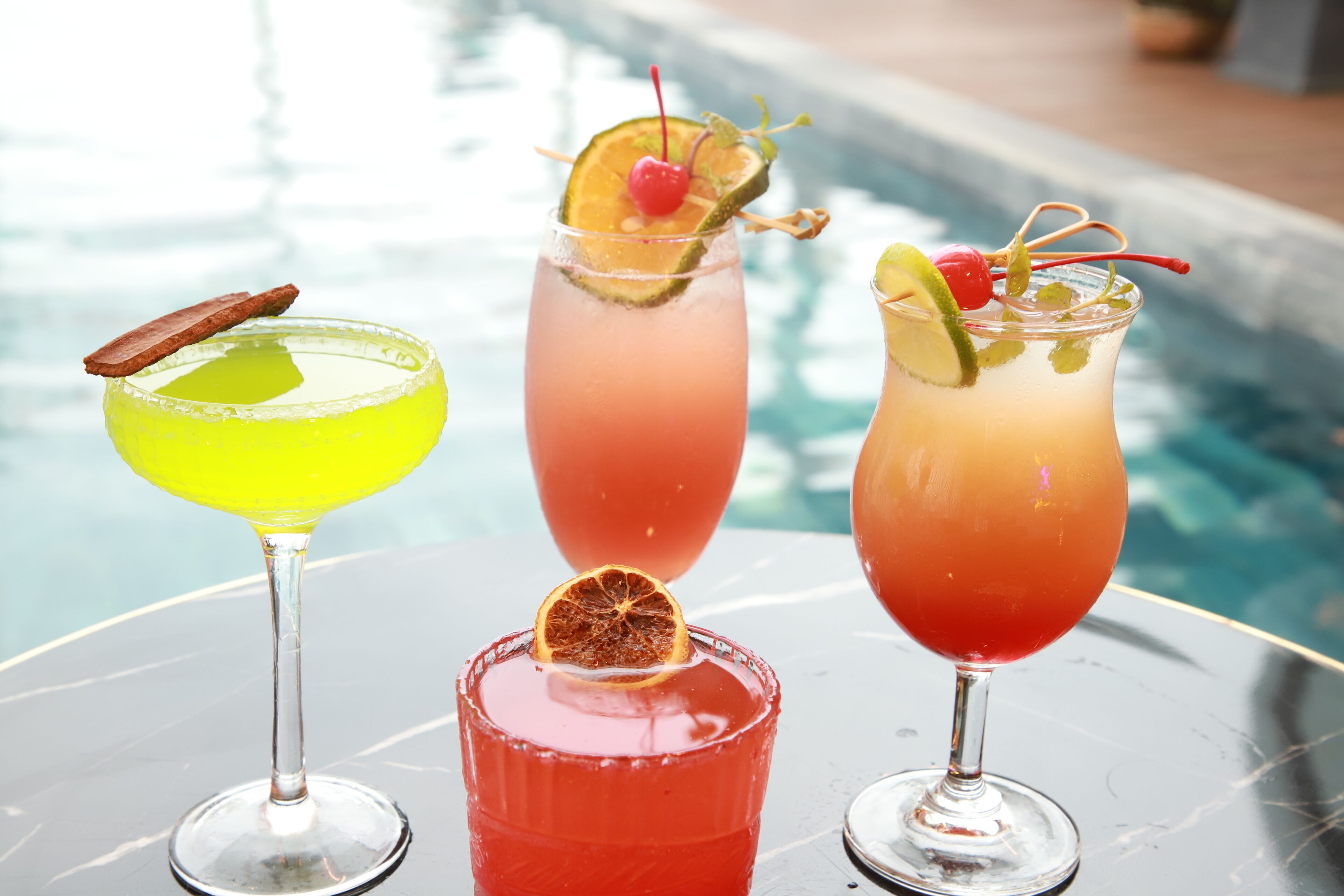 Three cocktails on a table by a pool.