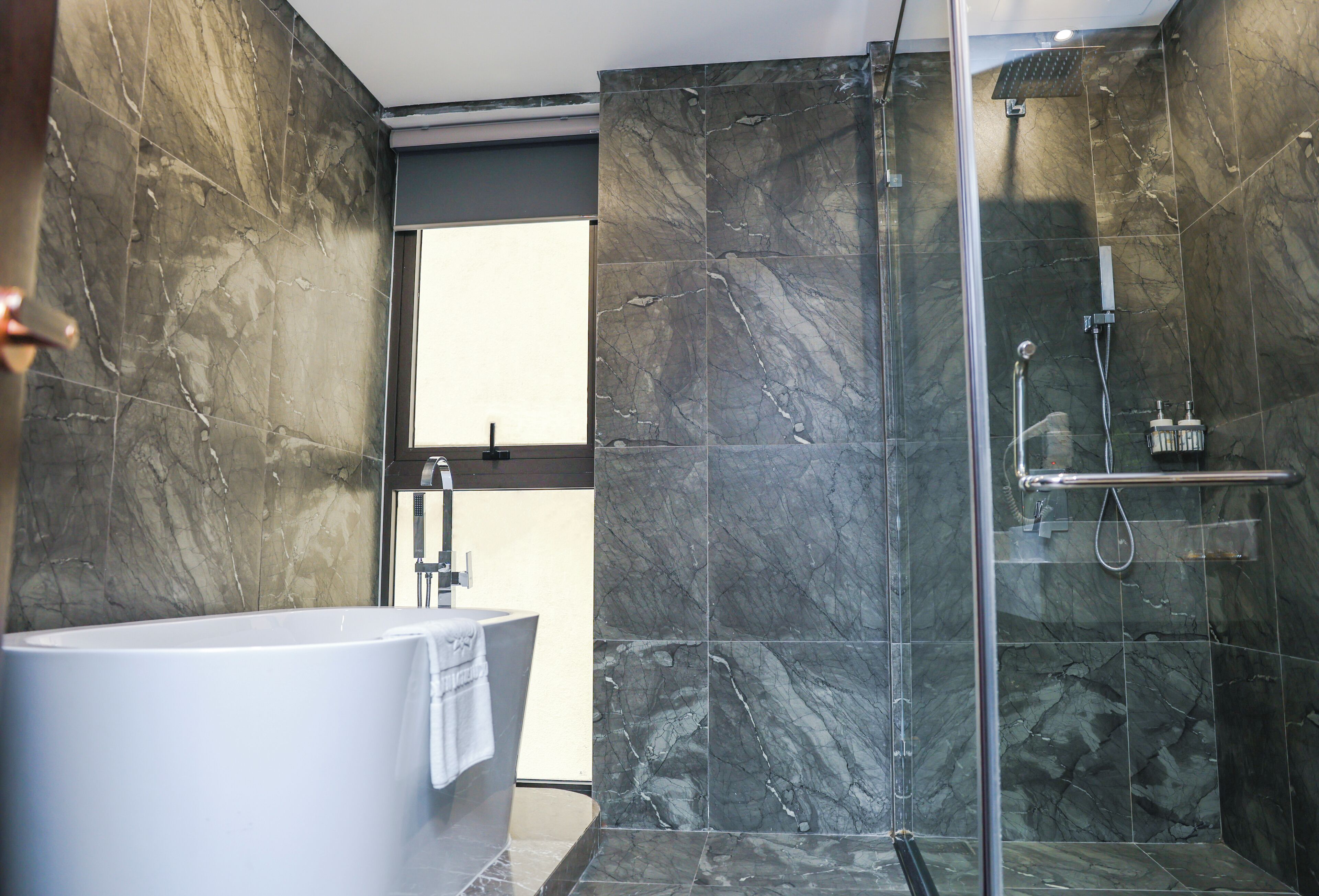 Une salle de bain moderne avec une baignoire sur pieds, une douche à parois de verre et des murs en marbre.