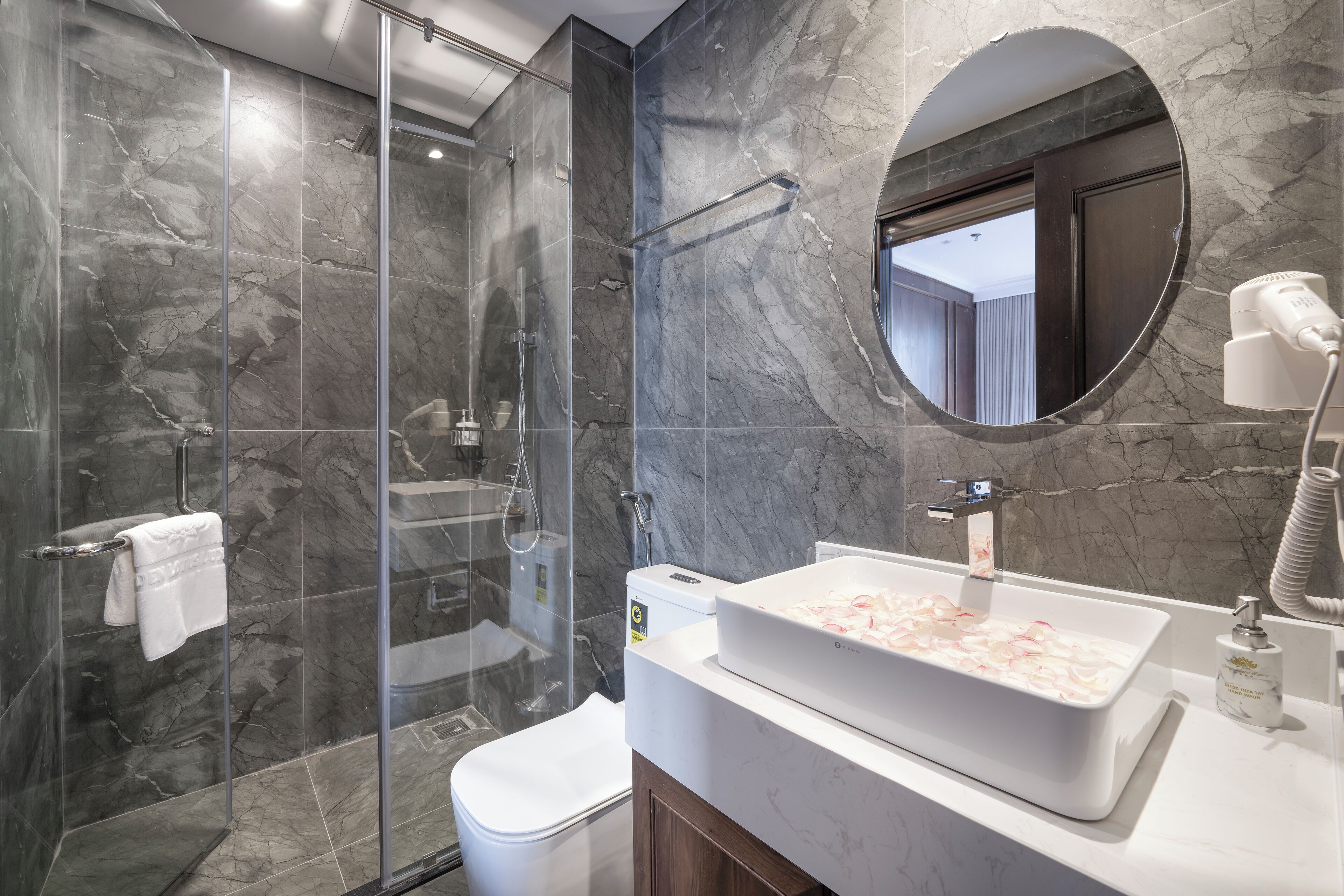 Ein modernes Badezimmer mit einer begehbaren Glasdusche, einem weißen Waschbecken mit Marmorplatte und einem runden Spiegel darüber.