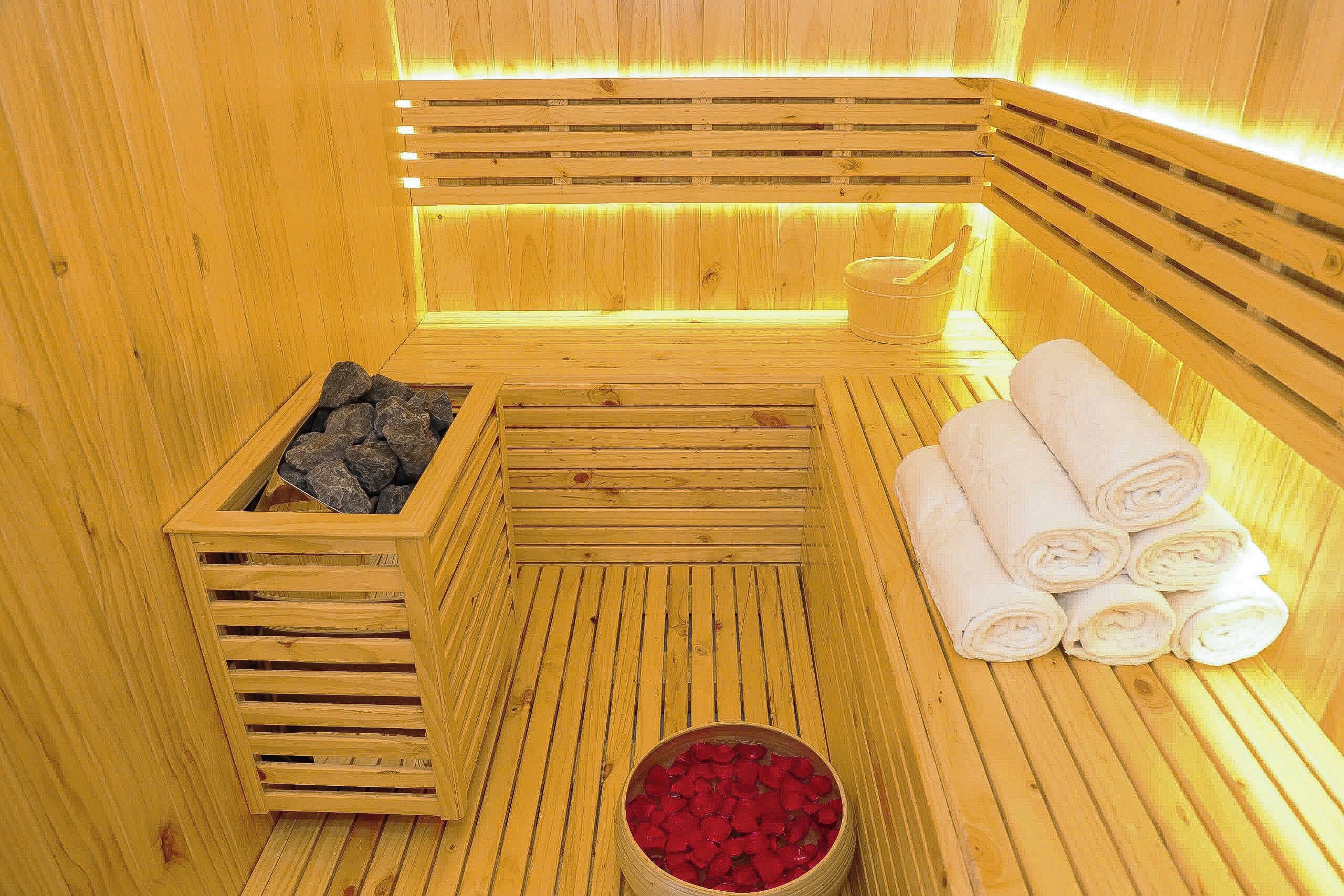 A wooden sauna with benches, a stone-filled container, and a bowl of red stones.