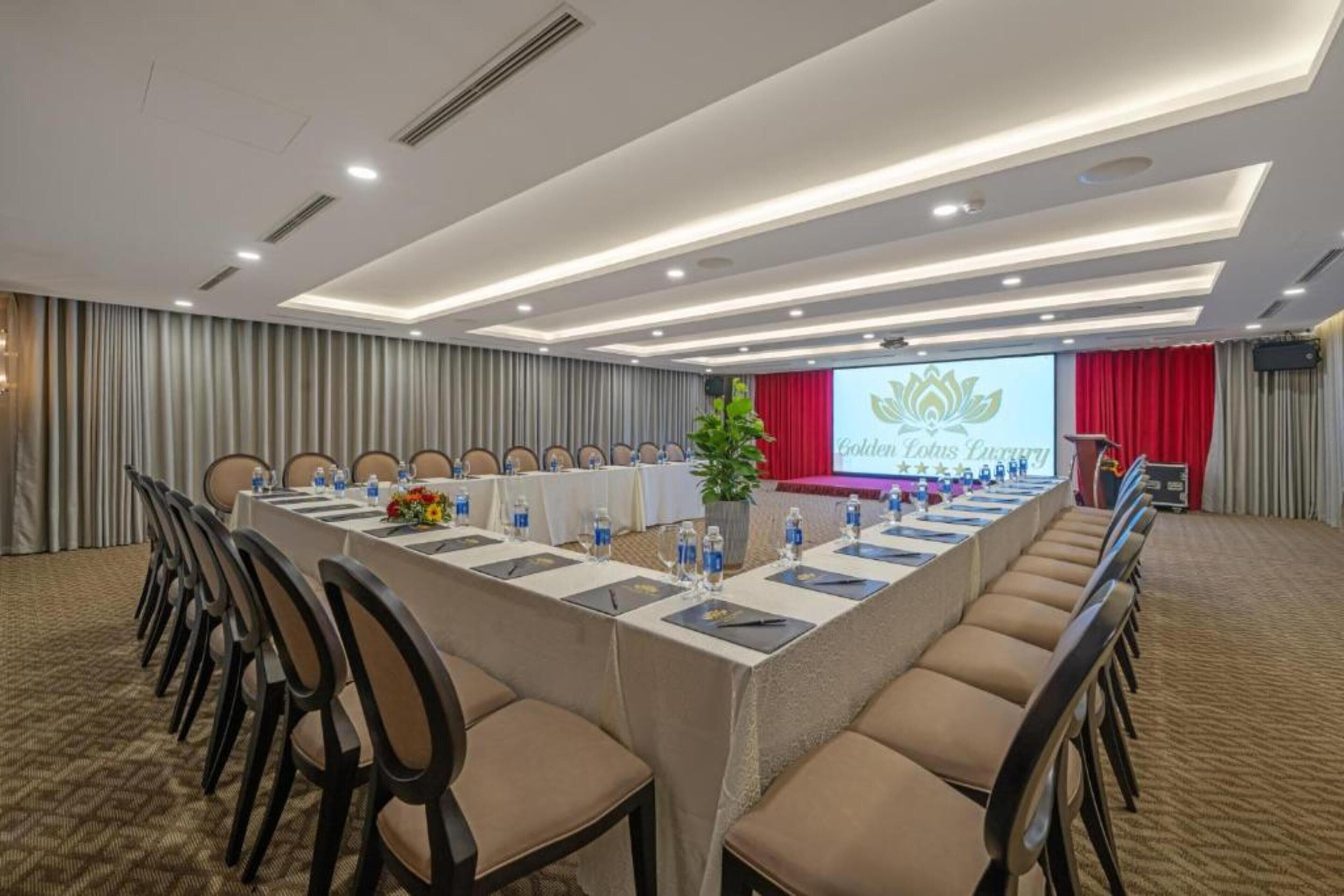 A conference room with a long table, chairs, and a stage with a presentation screen.