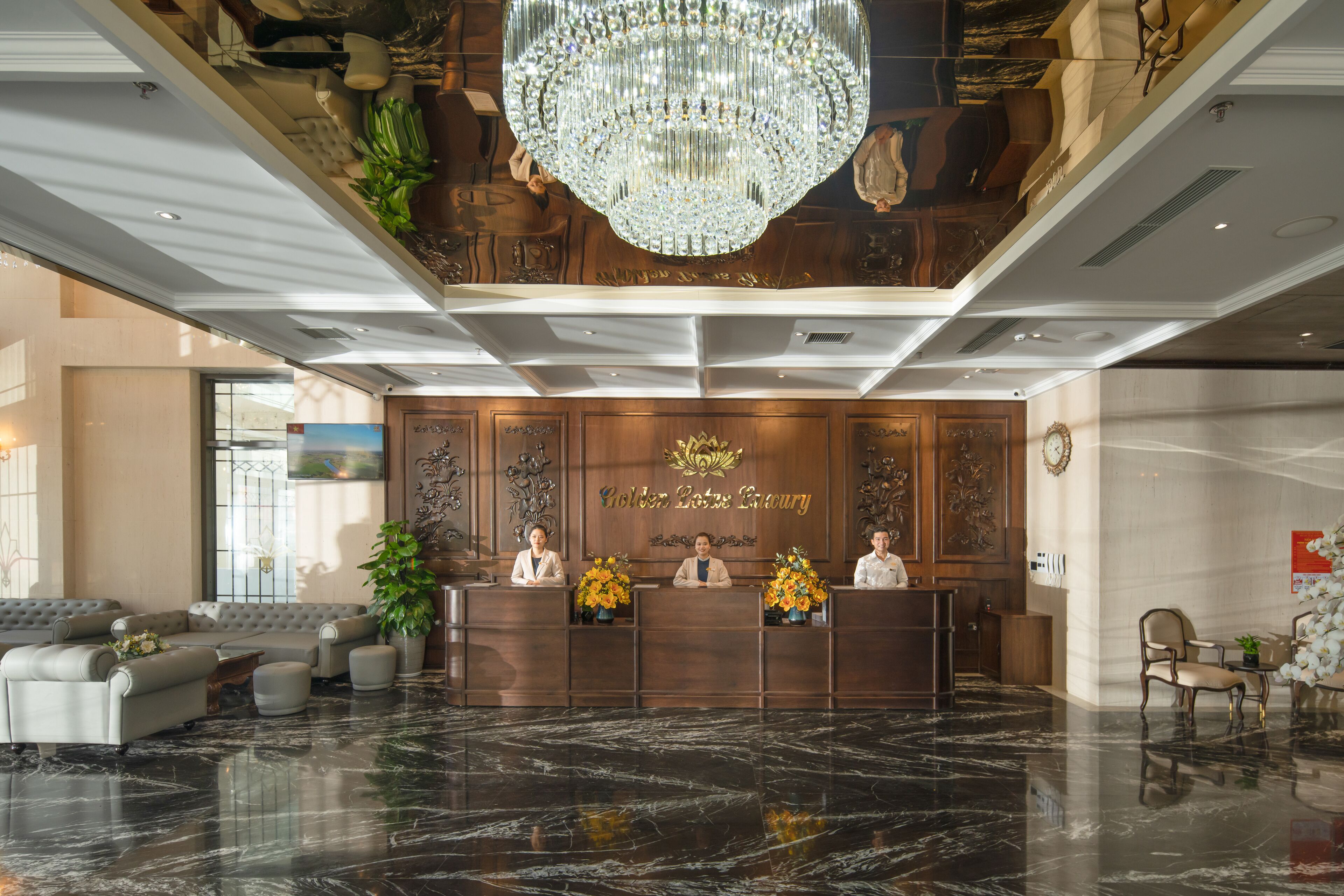 En hotellobby med ett marmorgolv, en stor kristallkrona och en receptionsdisk där tre anställda arbetar.