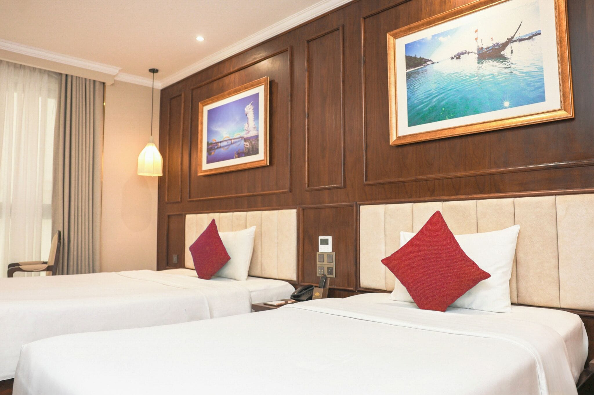A hotel room with two beds, a nightstand, a lamp, and a painting on the wall.