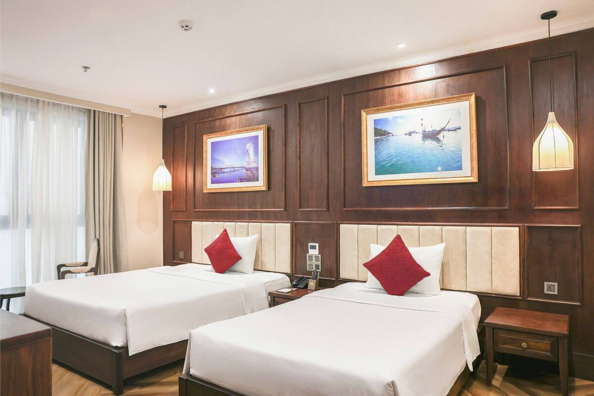 A hotel room with two beds, wooden paneling, a large window with curtains, and framed pictures on the wall.