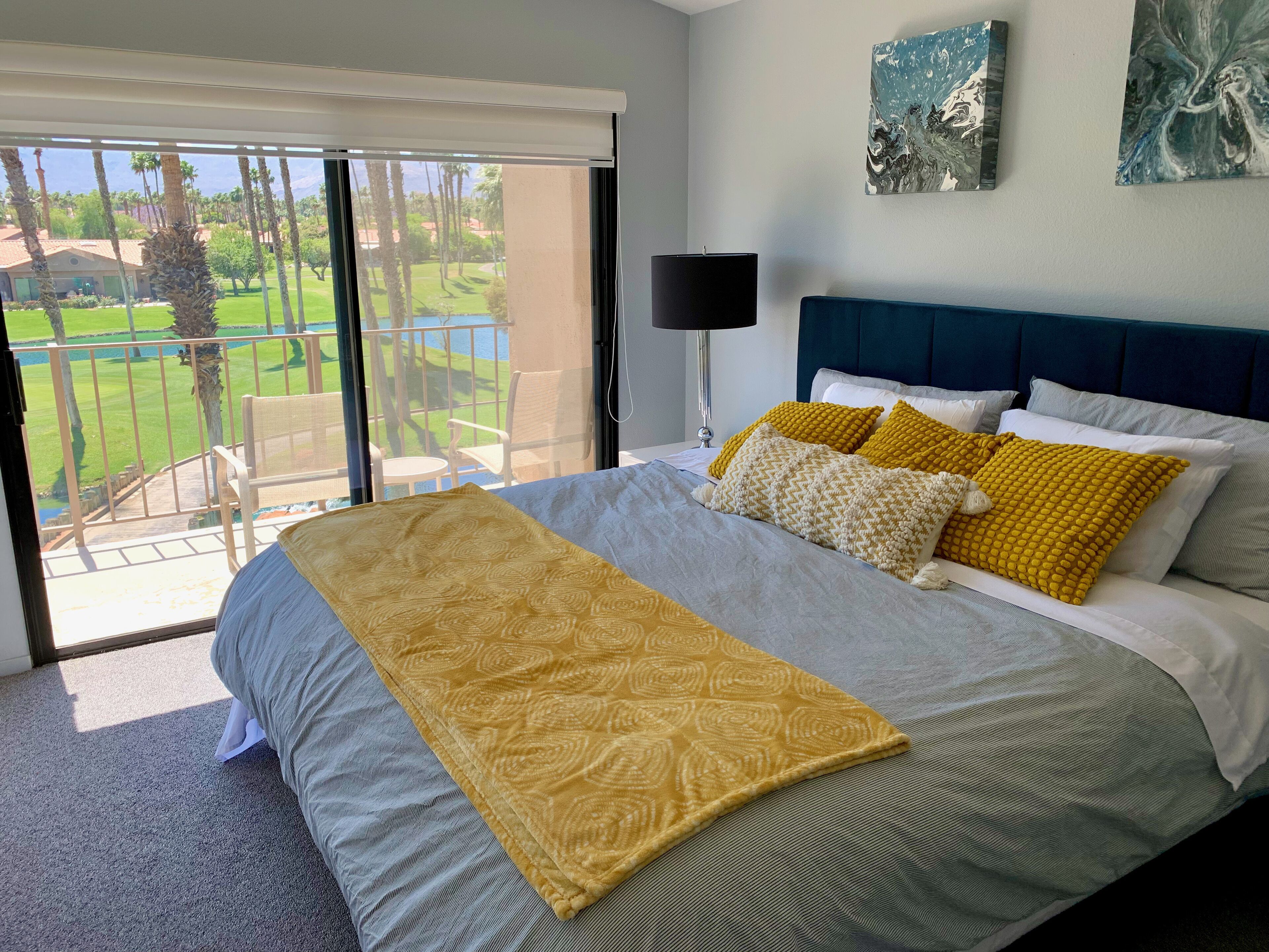 Une chambre avec un grand lit, une vue sur une pelouse verdoyante et des palmiers, et un balcon.