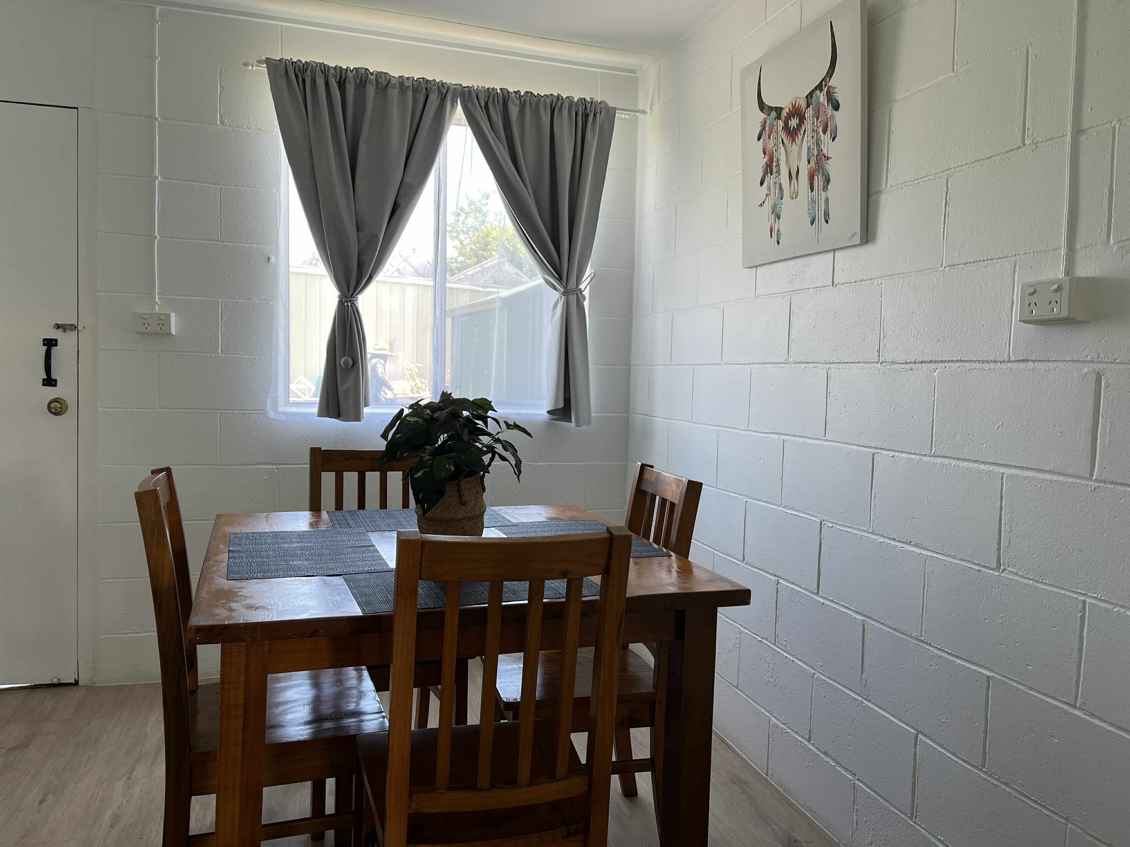 A dining area with a wooden table and chairs, a potted plant, and a window with curtains.