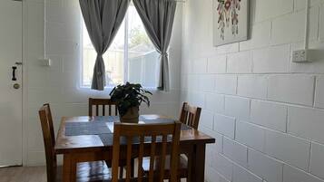 A dining area with a wooden table and chairs, a potted plant, and a window with curtains.