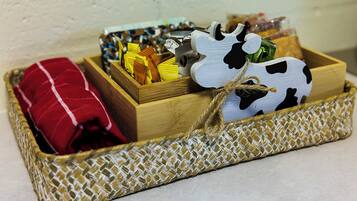A wooden basket with a woven base containing a red pillow, a cow-shaped container, and a box with yellow items.
