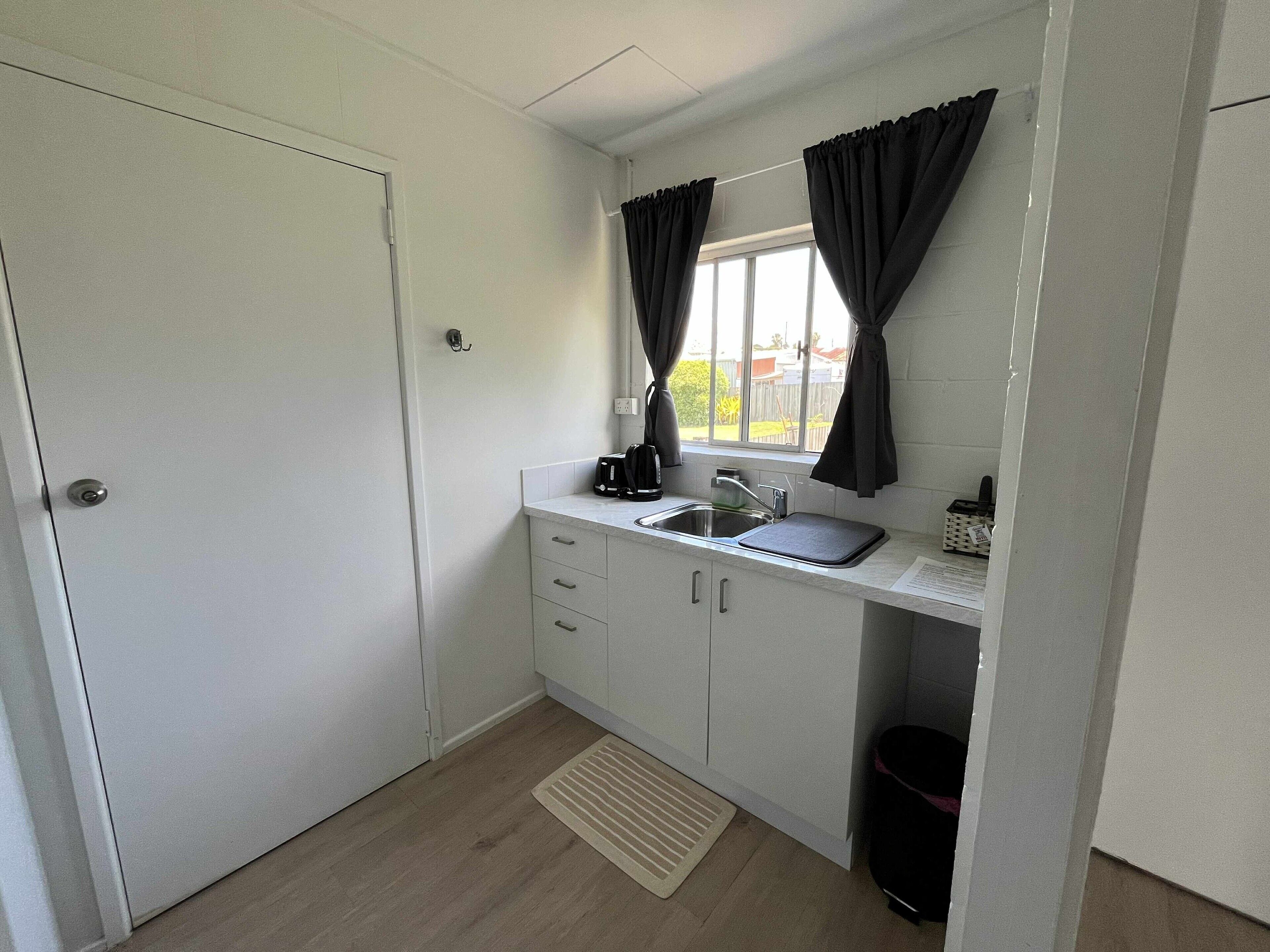 A compact kitchen with a sink, a coffee maker, and a window with curtains.