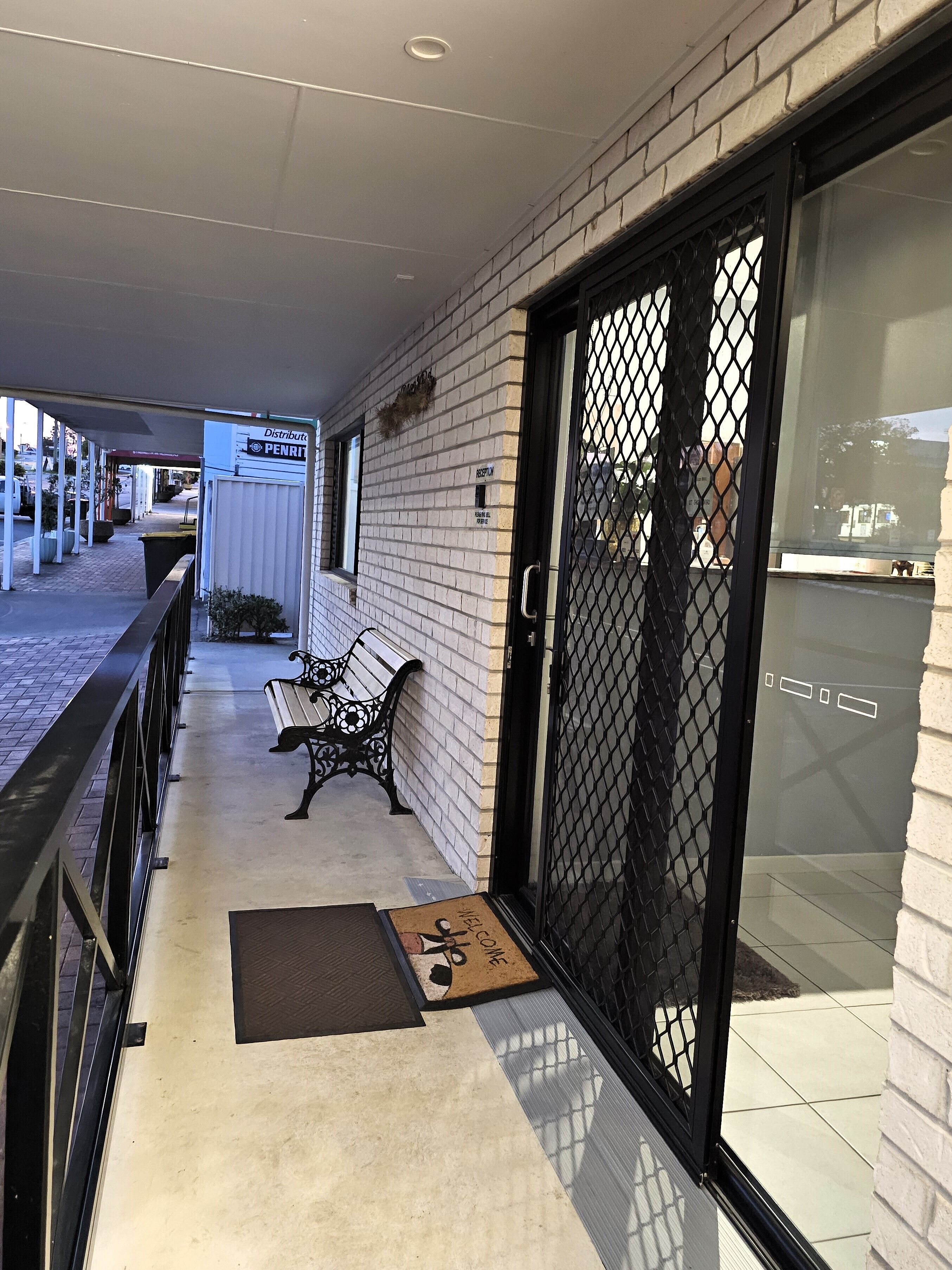Un passage couvert avec un banc, une porte dotée d’une grille de sécurité et un panneau indiquant une zone de distribution.