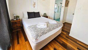 A neatly arranged bedroom with a bed, bedside tables, a bedside lamp, a wall-mounted air conditioner, and a framed picture. - Kilcoy Motel (Kilcoy)