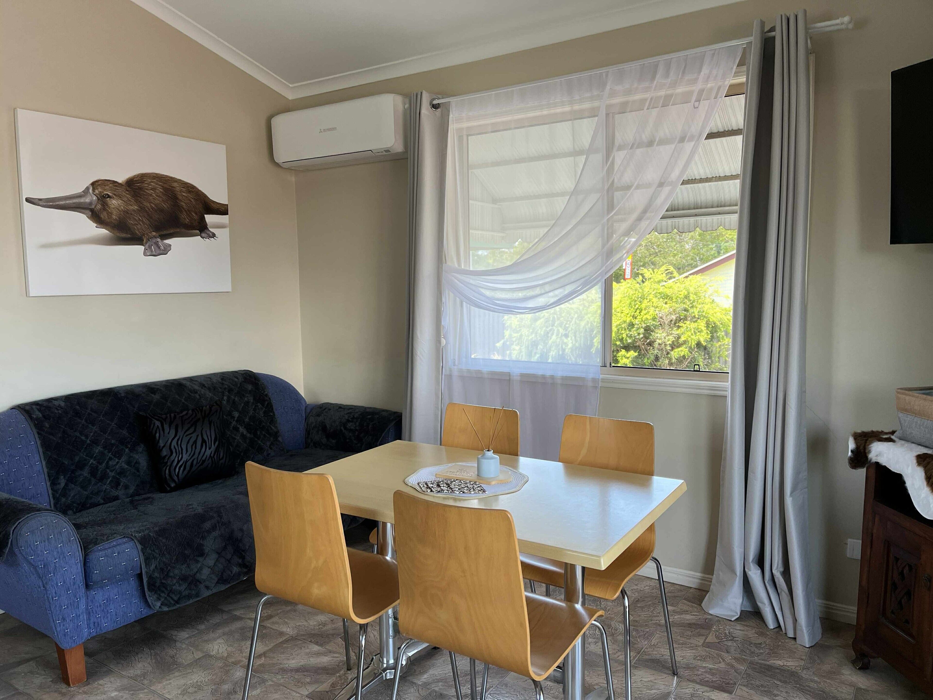 Ein Essbereich mit Tisch, Stühlen, einer Couch, einer Klimaanlage und einem Fenster mit Vorhängen.