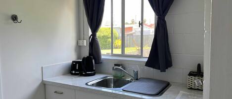 Una pequeña cocina con ventana, un lavamanos, una tetera y un tostador.