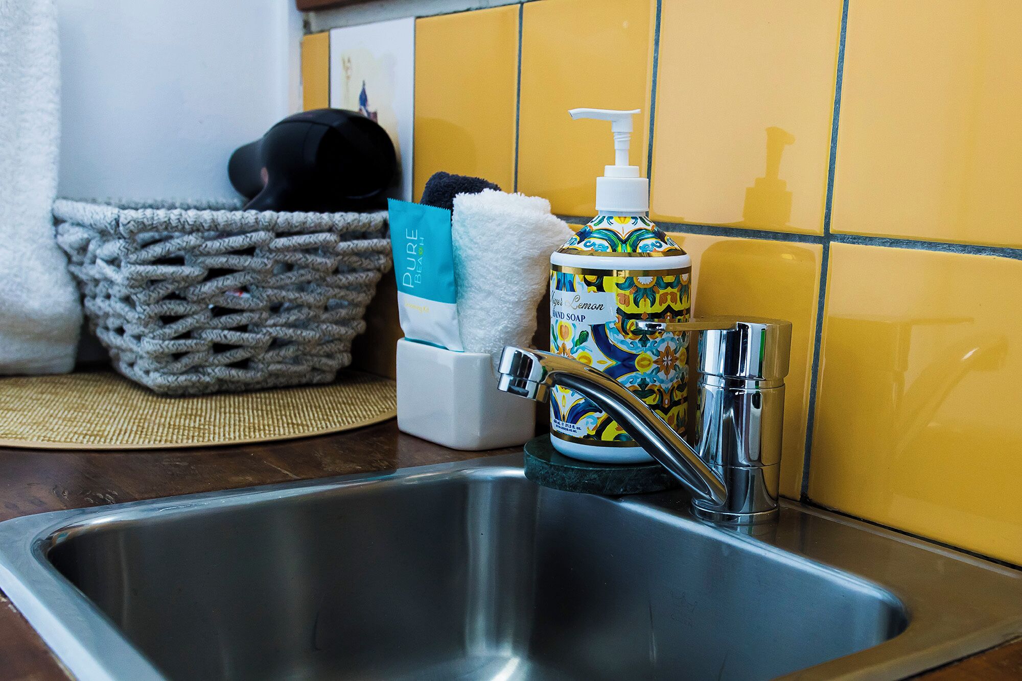 A kitchen sink with a soap dispenser, a woven basket, and a towel on a mat.