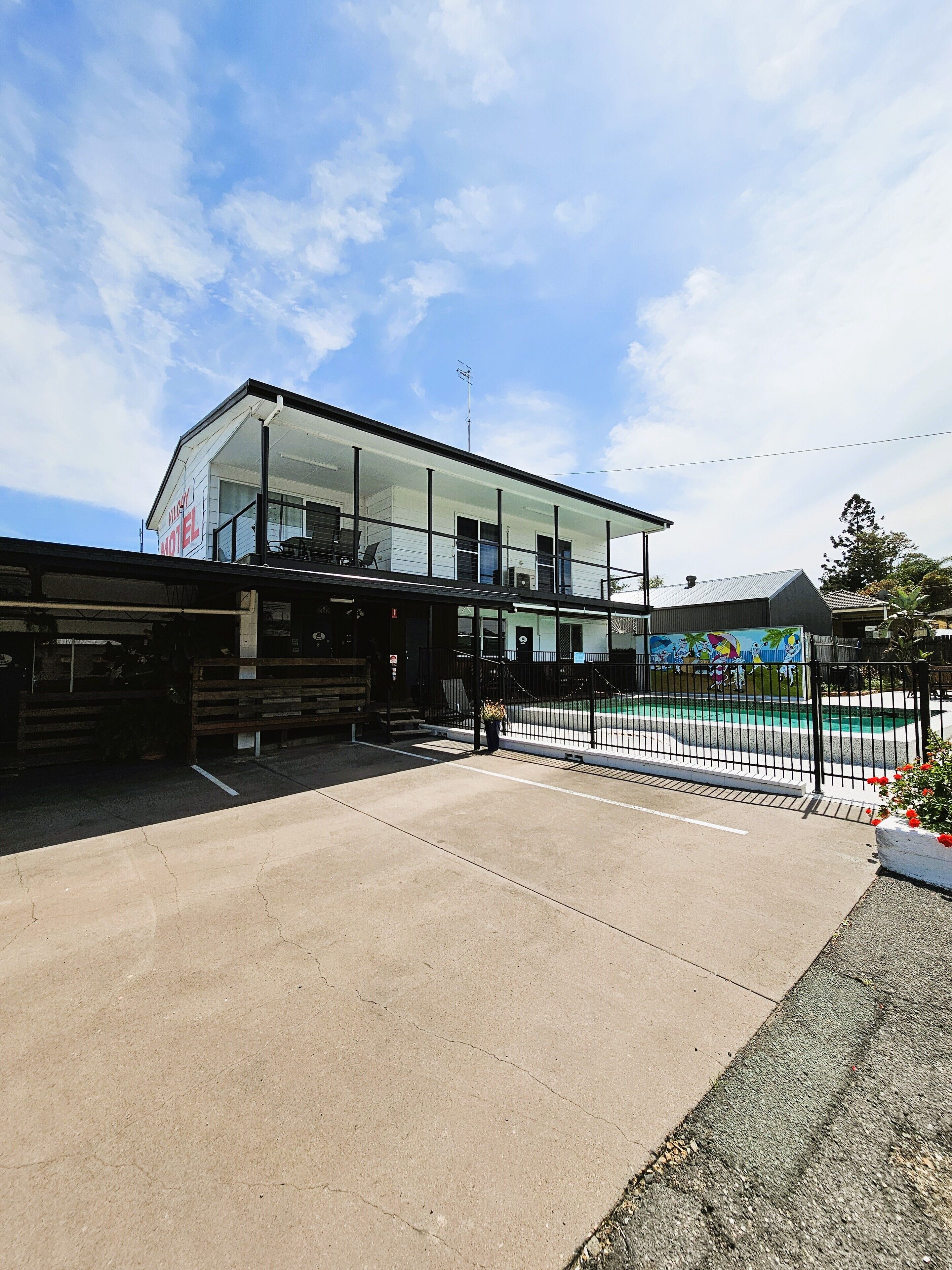 Un motel doté d’une façade en verre, d’un espace extérieur aménagé pour s’asseoir et d’un espace piscine.