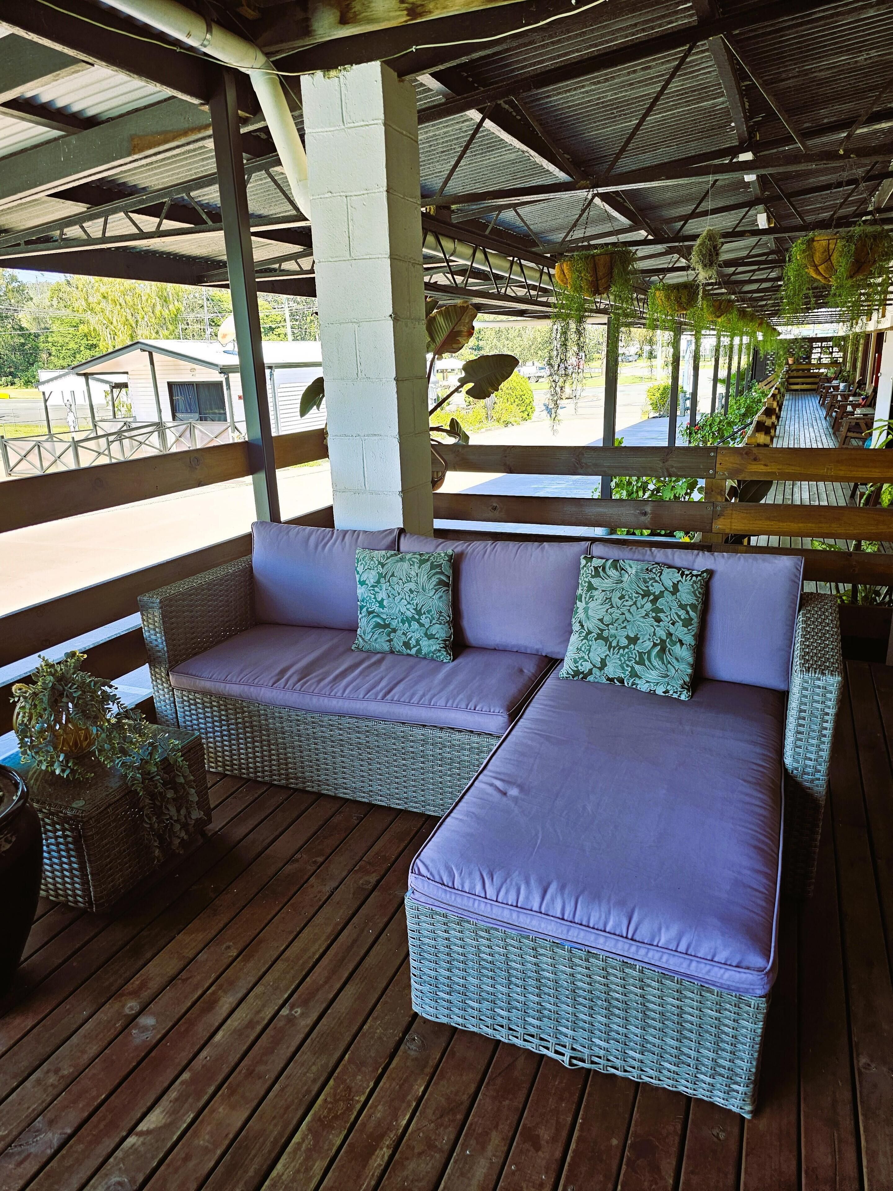 A covered outdoor seating area with wicker furniture and cushions, a wooden deck, and hanging plants.