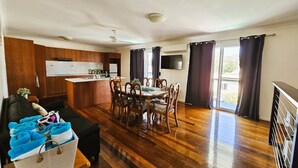 A spacious living area with a wooden floor, a dining table with chairs, a sofa, and a kitchen area with wooden cabinets and a TV. - Kilcoy Motel (Kilcoy)